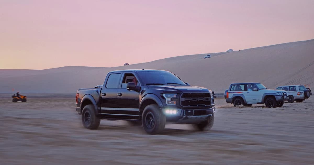 A 4x4 driving across the Sealine dunes at dusk, with other off road vehicles on the dune ridge behind