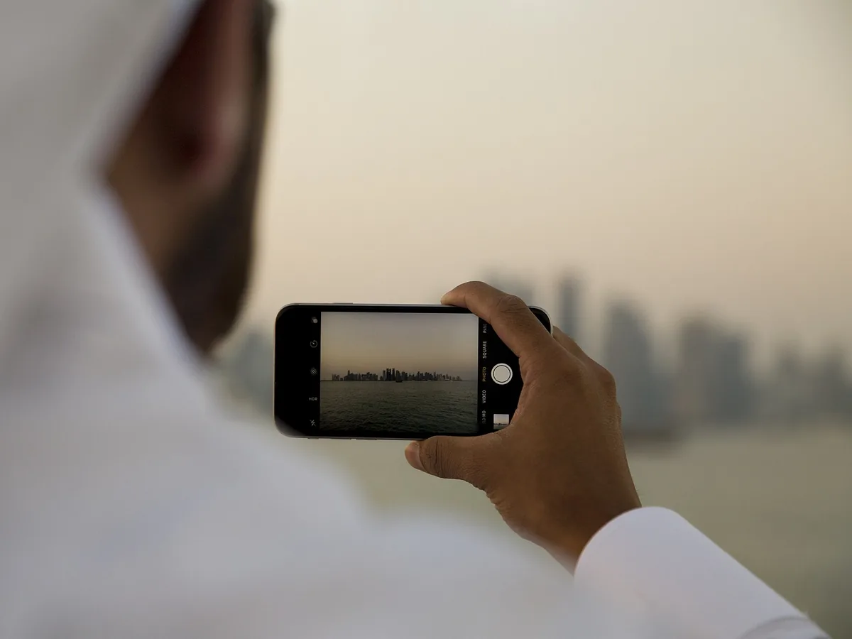 Resident holding a smartphone to photograph the Doha skyline across the bay