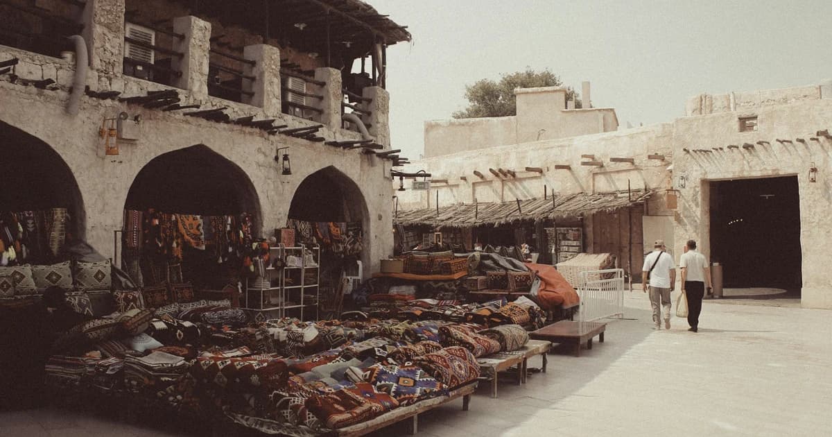 Carpet and textile stalls under stone arches in a lane at Souq Waqif, Doha